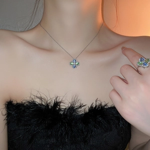 Close-up of a silver four-leaf flower necklace with blue and green gemstones on a model