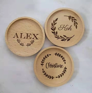 Close-up of circular wooden coasters with custom laser-engraved names and leaf patterns