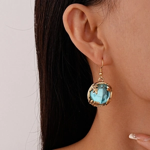 Detailed close-up of retro gold leaf earrings with round blue crystal on a model