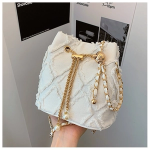 Close-up of white woven bucket bag featuring diamond quilted texture and golden chain strap