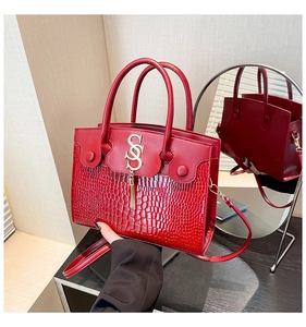 Detail of red crossbody bag featuring crocodile texture and golden tassel ornament