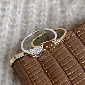 Close-up of gold and silver bear rings on brown crocodile leather and white knit background