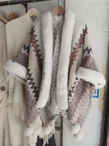 Detailed close-up of knitted poncho featuring white faux fur collar and pom-pom tassels