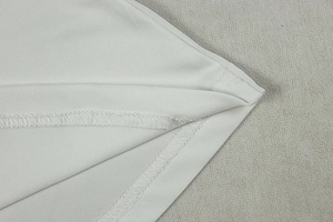 Detail of clean hemline stitching and fine white knitted fabric texture on the dress