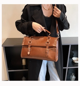 Close-up of vintage brown satchel with rivet details and double buckles on black coat