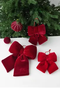 Close-up of red velvet Christmas bows and gold-lined ornaments on a green tree