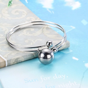 Silver stainless steel double-layer open bangle with metallic bead pendants on a book