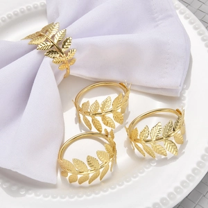 Set of four gold leaf-shaped metal napkin rings displayed on a white linen napkin and plate