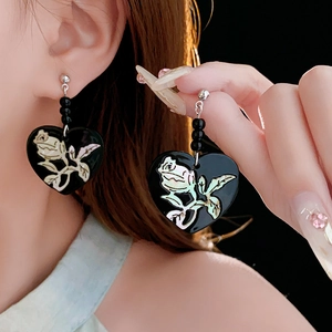 Detail of heart drop earrings with shell-effect rose pattern on black background