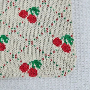 Close-up of knit fabric texture showing red cherry pattern on beige tote bag