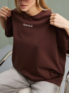 Nahaufnahme des weißen GALALÁ Aufdrucks auf einem dunkelbraunen Baumwoll-T-Shirt im Retro-Stil
