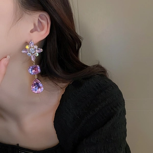 Close-up of elegant purple crystal water drop earrings with cross design worn by a model