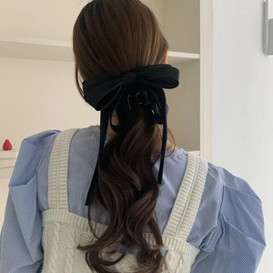 Detail of a large black satin bow hair claw clip styled on long wavy hair from behind
