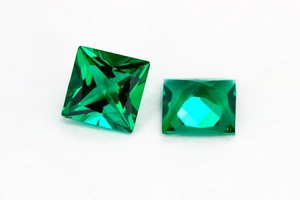 Macro shot of two princess cut emerald green gemstones with detailed facets and clarity