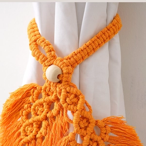 Close-up of orange hand-woven cotton curtain tieback with wooden bead and tassel detail