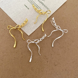 Close-up of elegant bow-shaped gold and silver earrings on a vintage aesthetic background