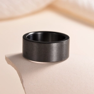 Macro detail of a 10mm wide matte black brushed titanium steel ring on a textured base