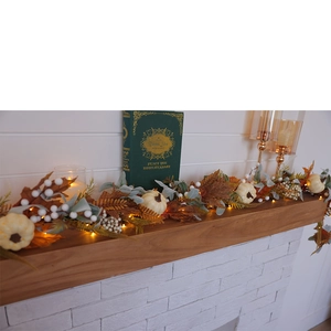 Detail of autumn garland with white pumpkins, berries and warm lights on wood mantel