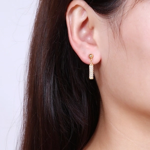 Fashionable 18K gold micro-pave cylindrical drop earrings worn by a model on white background