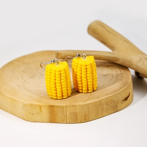 Macro detail of realistic yellow resin corn earrings with silver metal hooks on wood