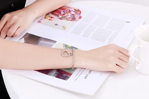 Silver hollow heart bracelet with zircons worn on wrist over a fashion magazine