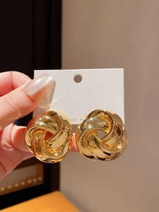 Macro shot of polished gold knot earrings with intertwined metal design on display card