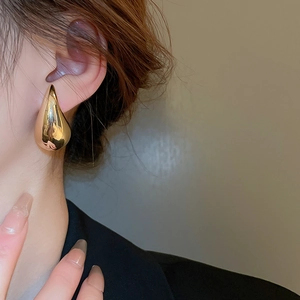 Close-up of a polished gold teardrop earring worn by a model for a minimalist style