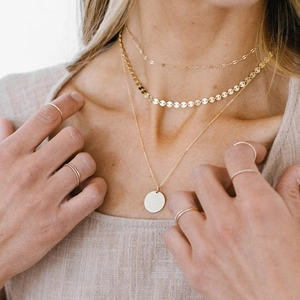 Close-up of three layered gold necklaces with disc pendant and six thin rings on model