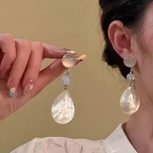Detailed view of elegant pearlescent drop earrings on model with iridescent shell texture