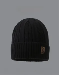 Detail view of black cable knit beanie featuring thick lining and brown leather patch