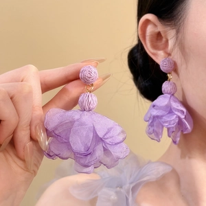 Detailed macro view of lavender chiffon flower earrings with raffia accents worn by model.