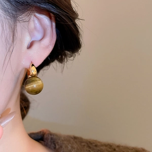 Close-up of a model wearing golden hoop earrings with tiger eye stone bead pendants