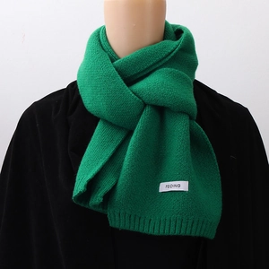 Close-up of green knitted winter scarf with white label detail on a model