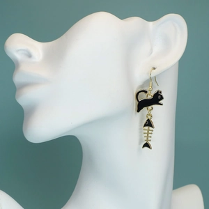 Detailed view of cat and fishbone drop earrings in gold and black on a model