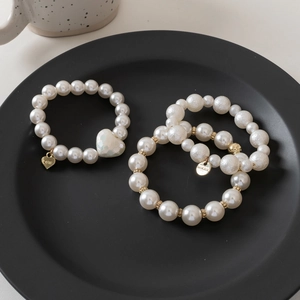 Detailed view of triple-layered pearl hair ties with a white heart charm on a black plate