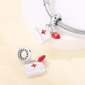 Detail of silver medical first aid kit bead and red heart charm on snake chain bracelet