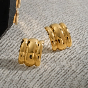 Close-up of polished gold-finished ribbed hoop earrings on a light textured fabric background