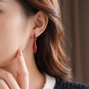 Elegant red fluid-shaped dangle earrings in minimalist modern art style on female model