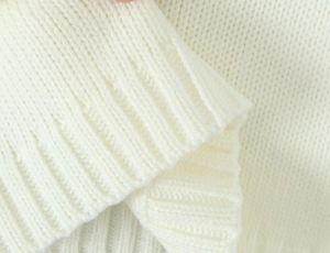 Close-up of premium white knit sweater detailing ribbed cuffs and high-density texture