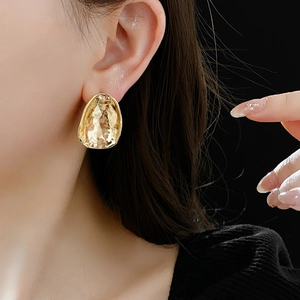 Close-up of a model wearing gold irregular hammered metal earrings with a textured surface