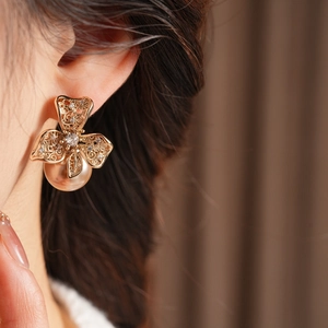 Détail d'une boucle d'oreille fleur dorée avec zircon et perle portée sur l'oreille
