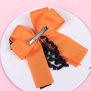 Detail view of orange satin bow hair clip with black wavy ribbon and metal alligator clip