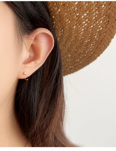 Close-up of elegant gold S925 silver ear studs worn by a model with a straw hat background