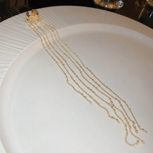 Detail of gold chain tassel ear cuff with long metallic fringe on a white textured plate