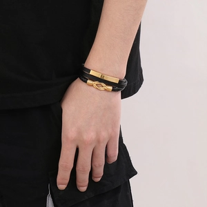 Détail d'un bracelet multicouche en cuir tressé noir avec accents métalliques dorés