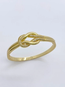 Detail eines goldenen Knoten-Armreifs mit einer Reihe funkelnder Zirkonia-Steine auf weißem Grund