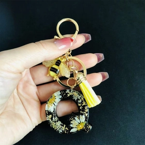 Detail of resin letter Q keychain with real dried flowers, gold bee charm and yellow tassel