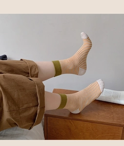 Détail de chaussettes en coton à rayures orange et revers côtelés vert olive sur bois