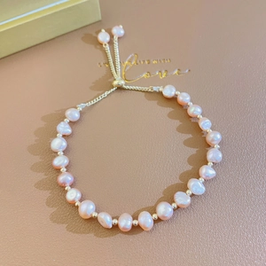 Detail of pink baroque pearls on a gold adjustable chain over brown leather