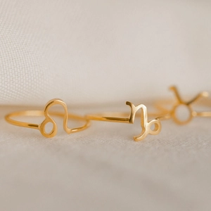 Golden stainless steel zodiac rings featuring Leo and Capricorn symbols on light fabric
